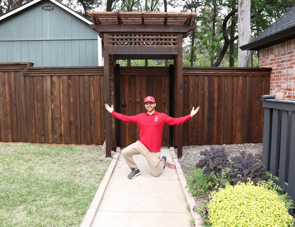 Austin Torres, owner of Jalapeno Fence Co., in front of a cedar fence with a pergola gate